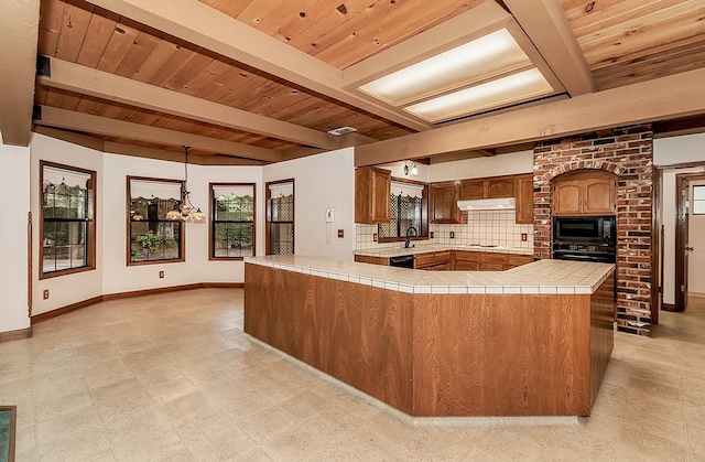 kitchen with black appliances, tile counters, under cabinet range hood, and baseboards