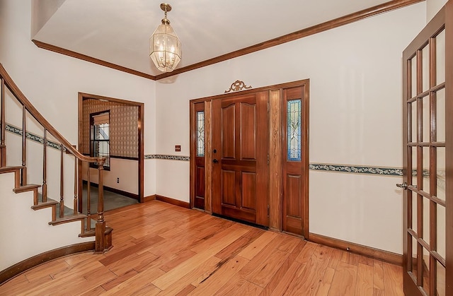 foyer entrance featuring stairway, a chandelier, light wood-style flooring, baseboards, and ornamental molding