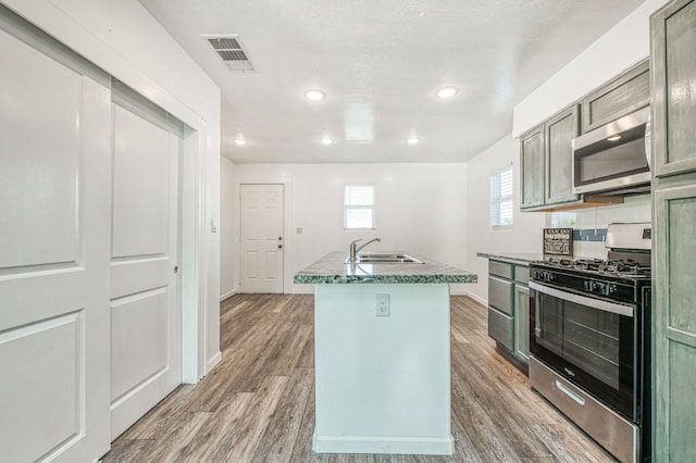 kitchen with backsplash, stainless steel appliances, a kitchen island with sink, sink, and wood-type flooring