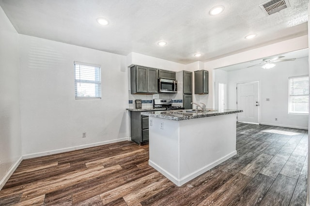 kitchen with dark stone countertops, a wealth of natural light, dark hardwood / wood-style flooring, and appliances with stainless steel finishes