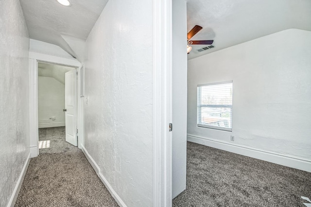 hallway with carpet flooring, a textured ceiling, and vaulted ceiling