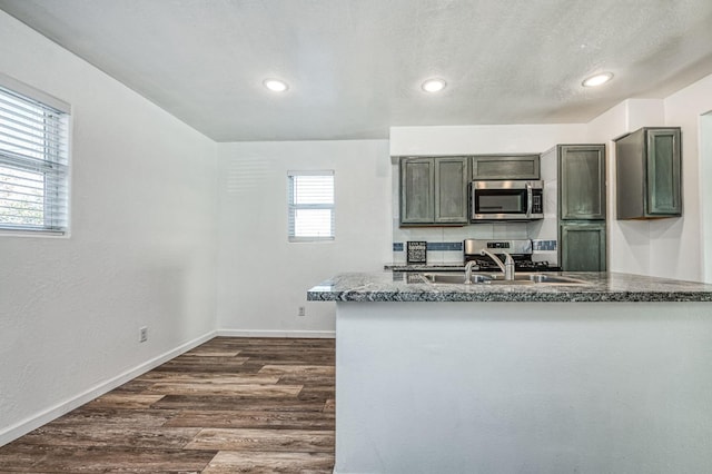 kitchen with sink, dark stone countertops, a textured ceiling, appliances with stainless steel finishes, and dark hardwood / wood-style flooring