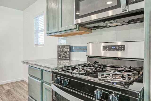 kitchen featuring stainless steel appliances, green cabinets, light stone counters, light hardwood / wood-style floors, and decorative backsplash