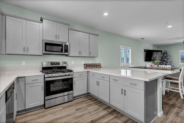 kitchen with gray cabinets, ceiling fan, stainless steel appliances, light hardwood / wood-style floors, and kitchen peninsula