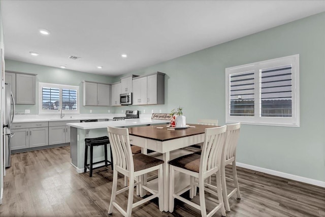 kitchen featuring a kitchen bar, sink, gray cabinetry, light wood-type flooring, and stainless steel appliances