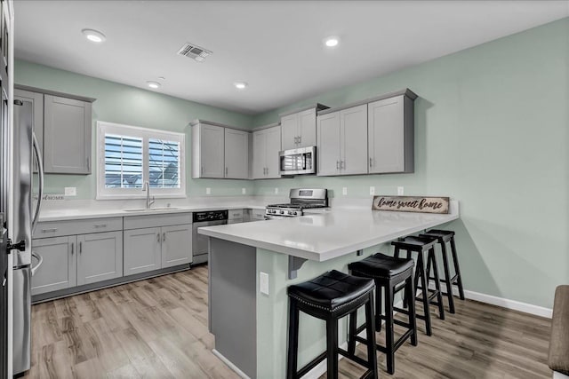 kitchen with sink, a breakfast bar area, kitchen peninsula, stainless steel appliances, and light hardwood / wood-style flooring