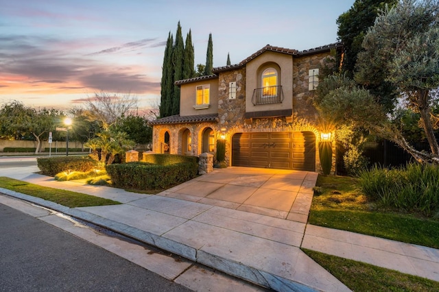 mediterranean / spanish home with a balcony, a garage, stone siding, driveway, and a tiled roof