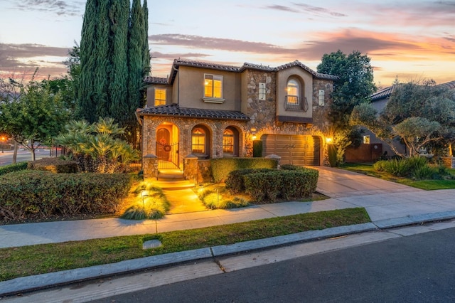 mediterranean / spanish-style home featuring stucco siding, concrete driveway, an attached garage, stone siding, and a tiled roof