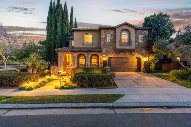 mediterranean / spanish-style house featuring stone siding, a tile roof, driveway, and stucco siding