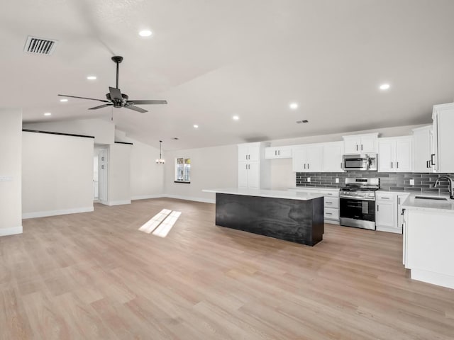 kitchen featuring white cabinetry, appliances with stainless steel finishes, a center island, vaulted ceiling, and sink