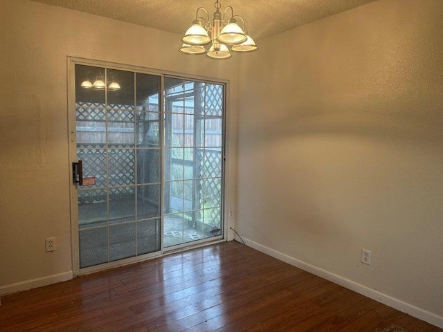 spare room featuring dark hardwood / wood-style flooring, a textured ceiling, and an inviting chandelier