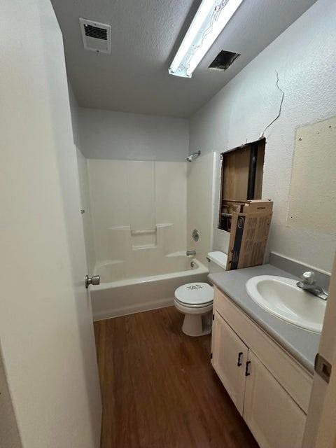 full bathroom with a textured ceiling, vanity, hardwood / wood-style flooring, washtub / shower combination, and toilet