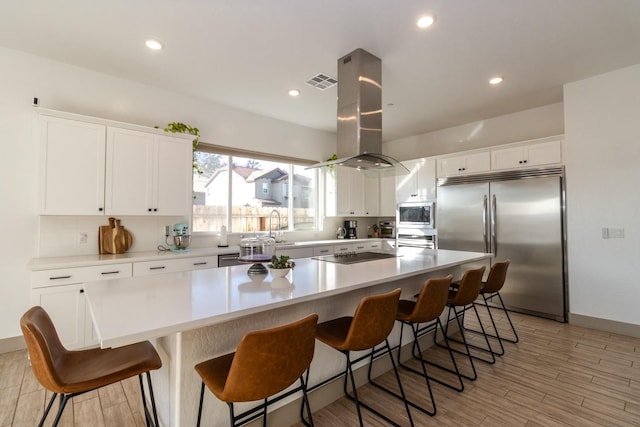 kitchen featuring white cabinets, a spacious island, built in appliances, light wood-type flooring, and a breakfast bar area