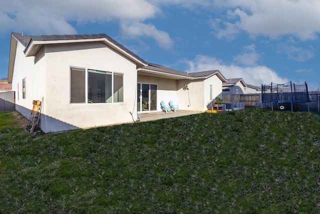 back of property featuring a trampoline, a patio, and a yard