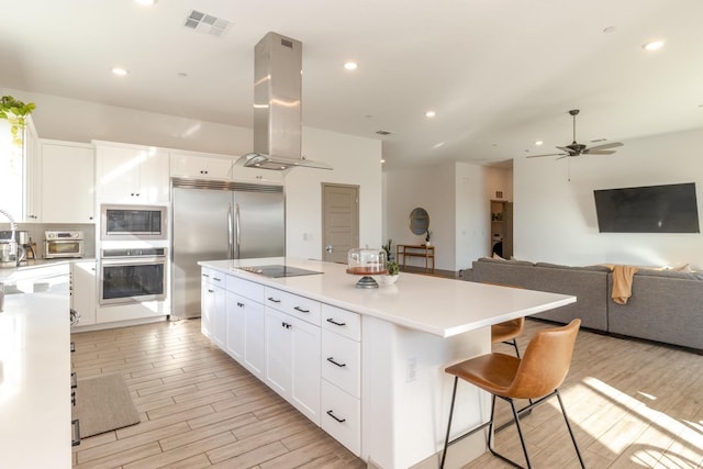 kitchen with island exhaust hood, black appliances, a center island, light hardwood / wood-style floors, and white cabinetry