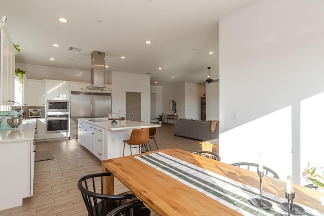 kitchen with island range hood, built in appliances, light wood-type flooring, a kitchen island, and white cabinetry