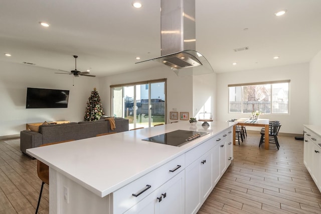 kitchen with black electric stovetop, island range hood, white cabinetry, and a wealth of natural light