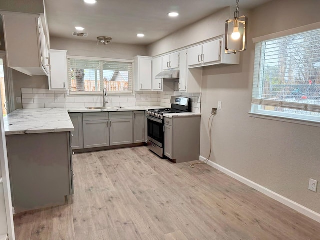 kitchen with visible vents, gas range, hanging light fixtures, under cabinet range hood, and a sink