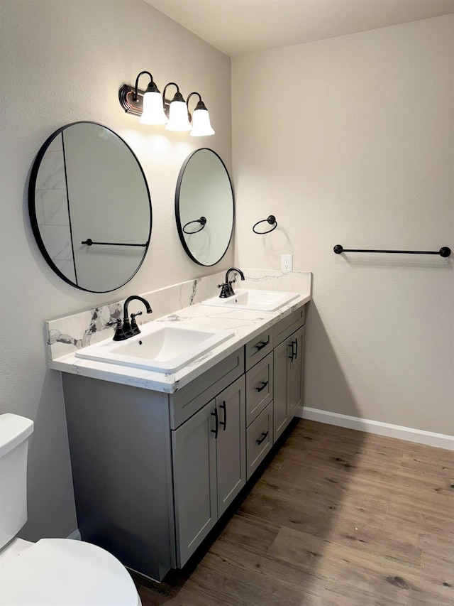 bathroom with double vanity, wood finished floors, a sink, and toilet