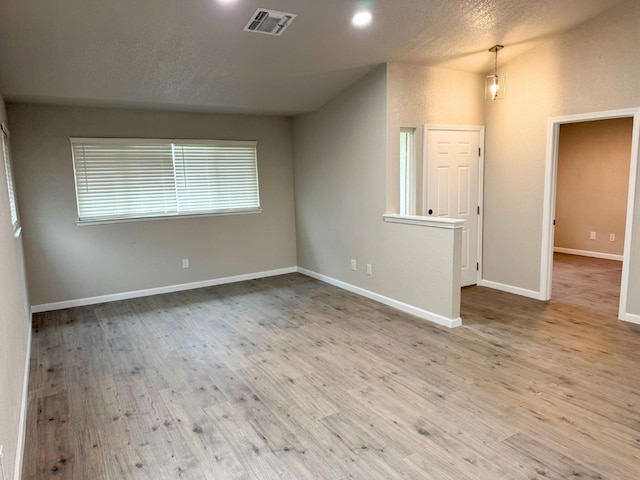 empty room featuring baseboards, visible vents, a textured ceiling, and light wood finished floors