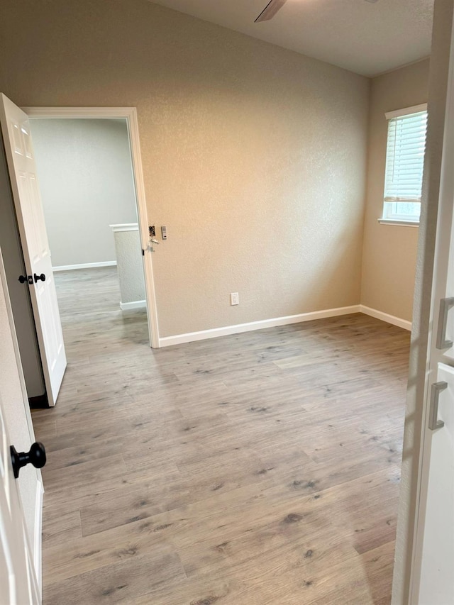 spare room featuring ceiling fan, light wood-type flooring, and baseboards