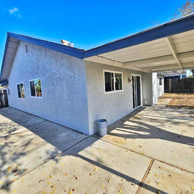 view of side of property with stucco siding, fence, a carport, and a patio