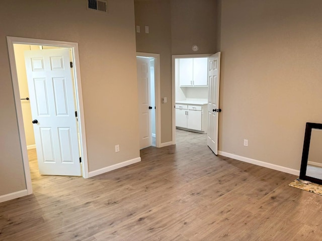 empty room with light wood-type flooring, baseboards, a towering ceiling, and visible vents