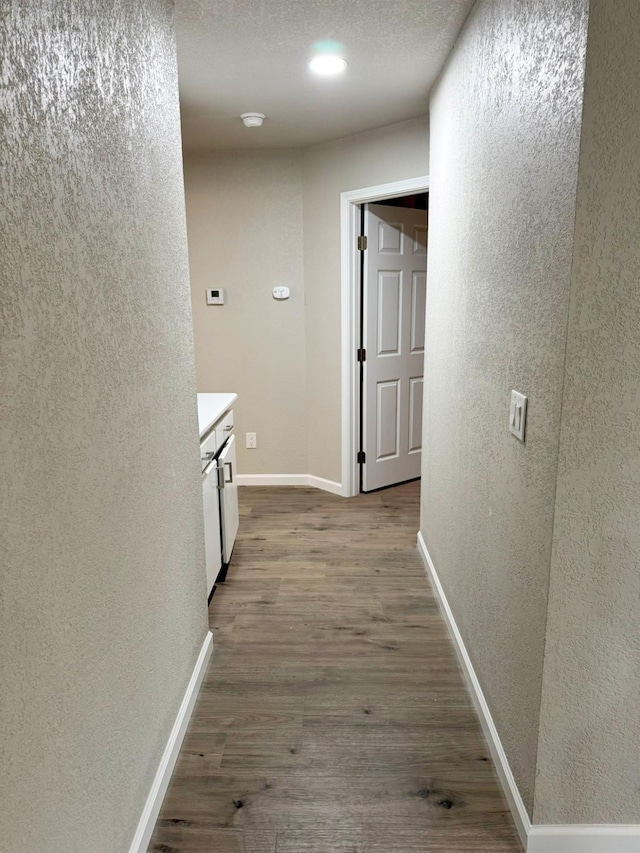 hallway with light wood finished floors, baseboards, a textured ceiling, and a textured wall