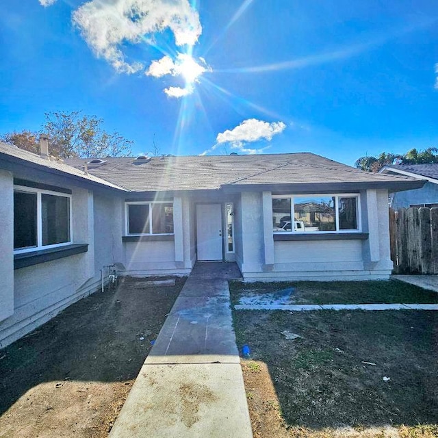 entrance to property with roof with shingles, fence, and stucco siding