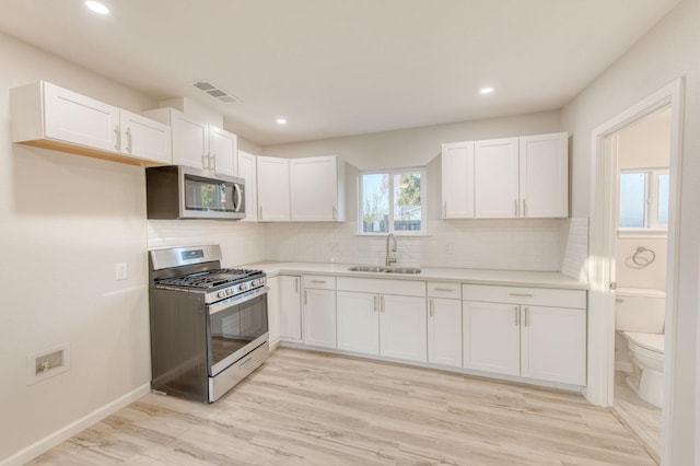 kitchen with white cabinets, stainless steel appliances, light hardwood / wood-style floors, and sink