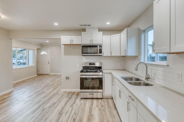 kitchen with a wealth of natural light, sink, stainless steel appliances, white cabinets, and light wood-type flooring