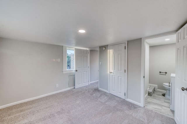 unfurnished bedroom with ensuite bathroom and light colored carpet