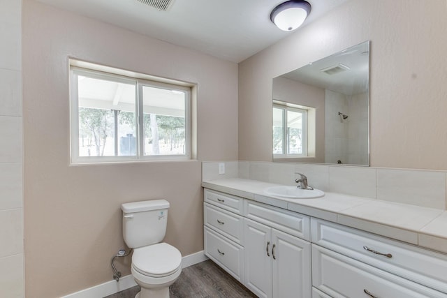 bathroom with a tile shower, hardwood / wood-style floors, vanity, and toilet