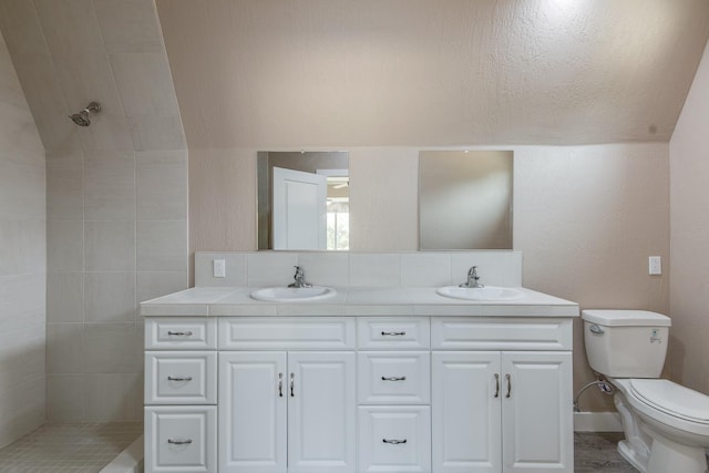 bathroom featuring toilet, a tile shower, vanity, and vaulted ceiling