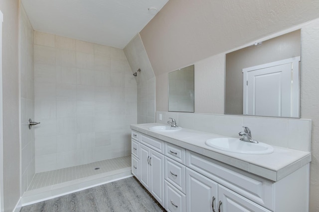 bathroom featuring hardwood / wood-style floors, vanity, a tile shower, and decorative backsplash