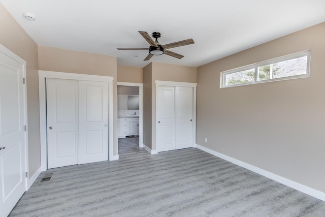 unfurnished bedroom with light wood-type flooring, two closets, and ceiling fan