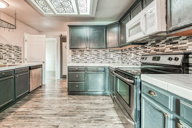 kitchen with tile countertops, backsplash, stainless steel appliances, and light hardwood / wood-style floors