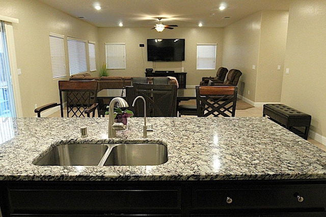 kitchen with light tile patterned flooring, an island with sink, sink, ceiling fan, and light stone counters