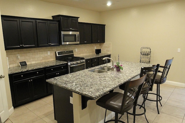 kitchen featuring a kitchen bar, sink, tasteful backsplash, a center island with sink, and appliances with stainless steel finishes