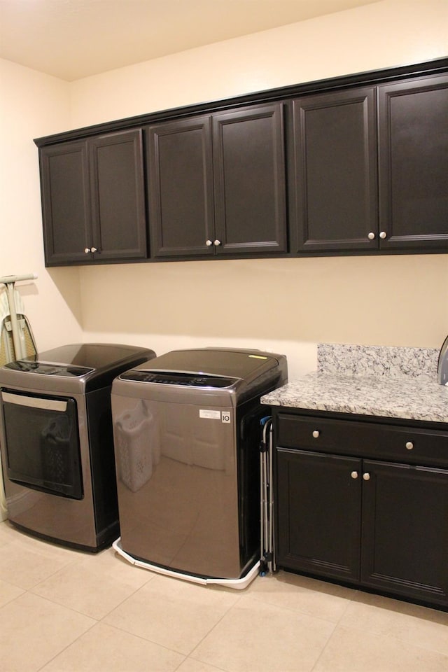 clothes washing area featuring light tile patterned flooring, cabinets, and washing machine and dryer