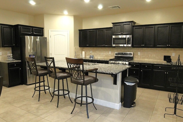 kitchen featuring stainless steel appliances, a kitchen bar, light stone countertops, and an island with sink