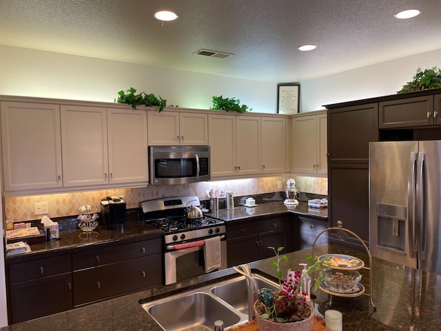 kitchen with sink, dark stone counters, a textured ceiling, white cabinets, and appliances with stainless steel finishes