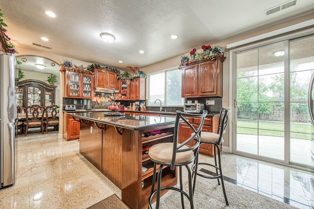 kitchen with a breakfast bar, a center island, a textured ceiling, and tasteful backsplash