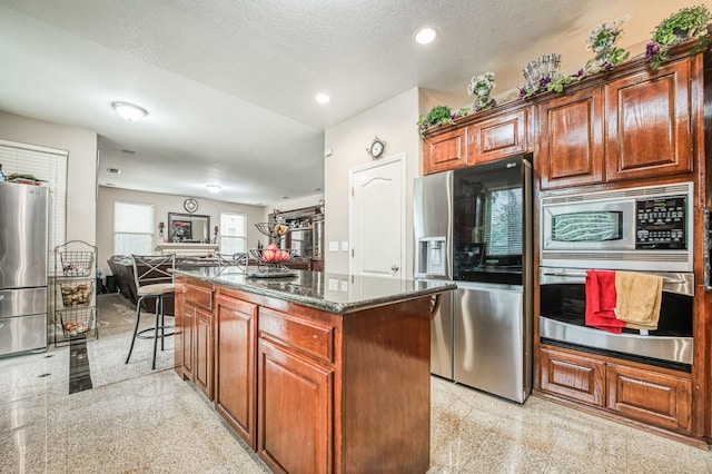 kitchen with a textured ceiling, a kitchen island, dark stone countertops, and stainless steel appliances