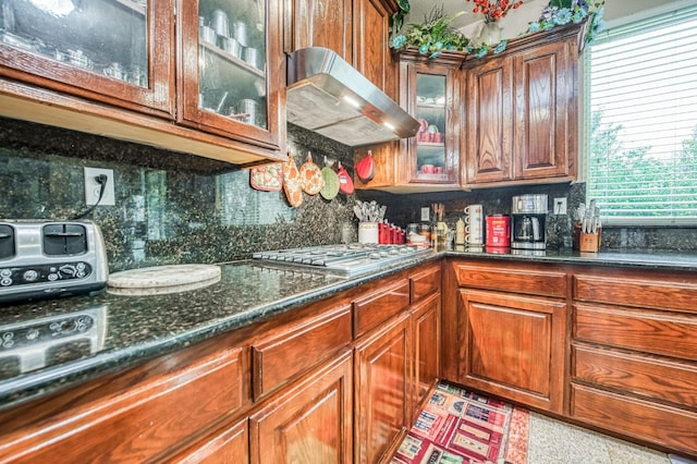 kitchen featuring backsplash, dark stone countertops, exhaust hood, and stainless steel gas cooktop