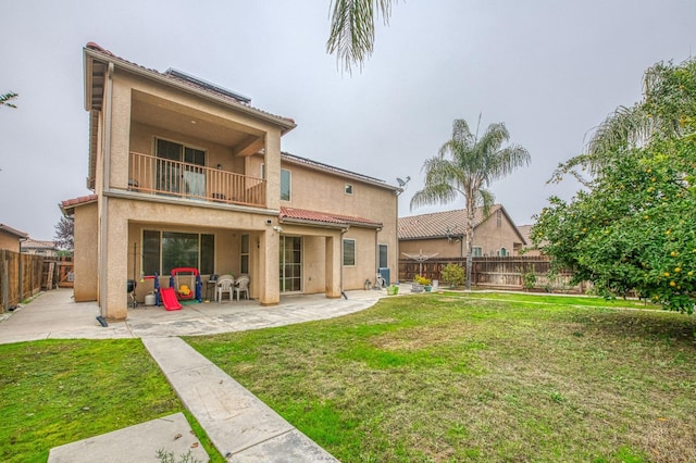 rear view of property with a patio, a balcony, and a lawn