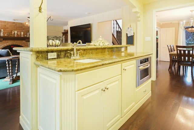 kitchen featuring dark hardwood / wood-style flooring, light stone counters, sink, oven, and an island with sink