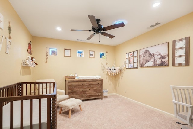 carpeted bedroom with ceiling fan and a crib