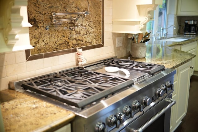 kitchen featuring decorative backsplash, stainless steel range, sink, stone countertops, and green cabinets