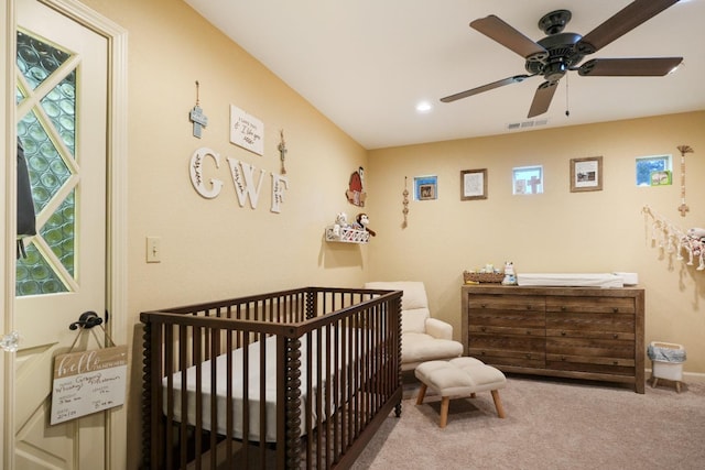 carpeted bedroom with a crib and ceiling fan